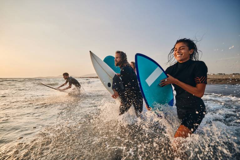 people running into ocean with surf boards