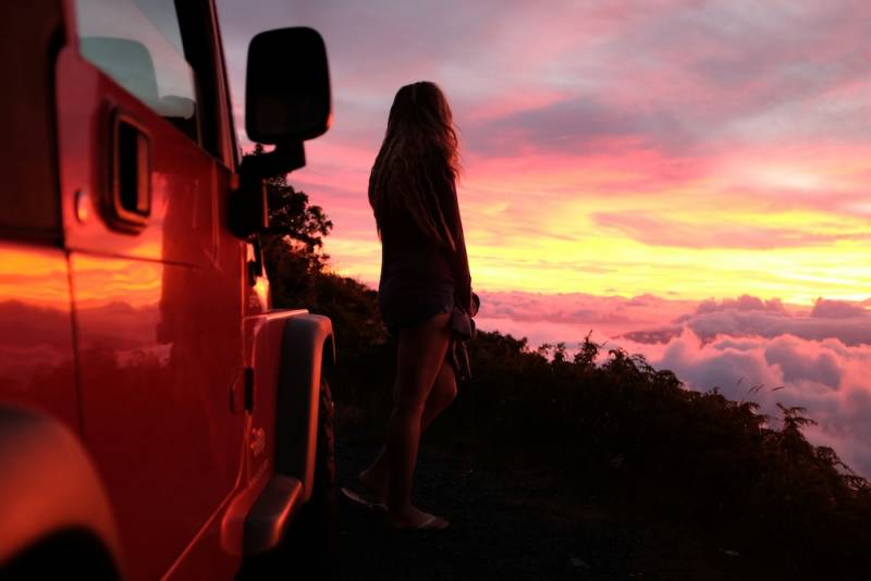 Woman in Hawaii with car looking at sunset